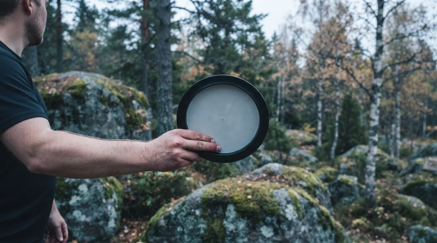 Spiller holder disken i forehand-grep med strak arm ut til siden, i skog med mosegrodde steiner.